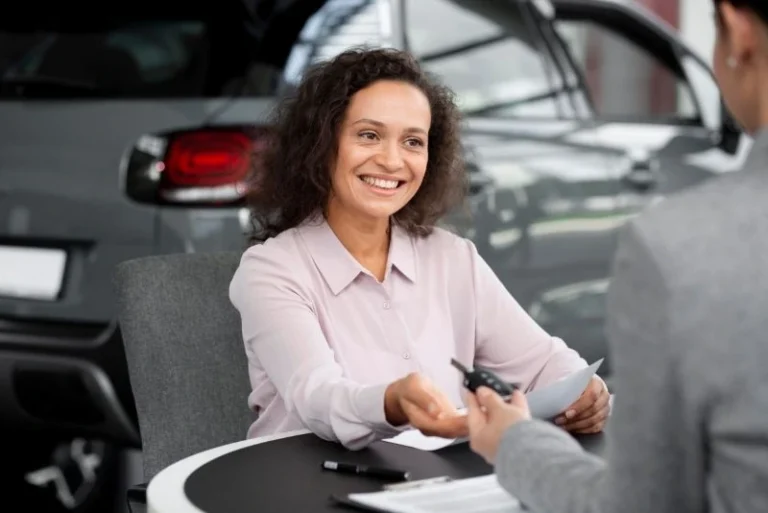 Smiling woman receiving car keys from a dealer at a showroom desk, a positive outcome after applying for a car loan.