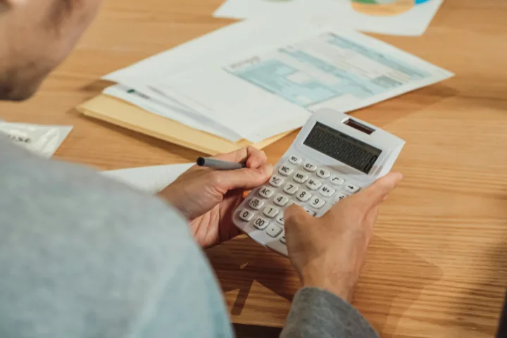 Person holding a calculator with a pen over financial reports on a wooden desk — common for self-employed borrowers.