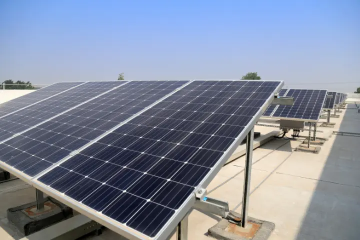 Rows of solar panels on metal frames installed on a flat rooftop under a clear blue sky, a typical investment funded through green assets finance.